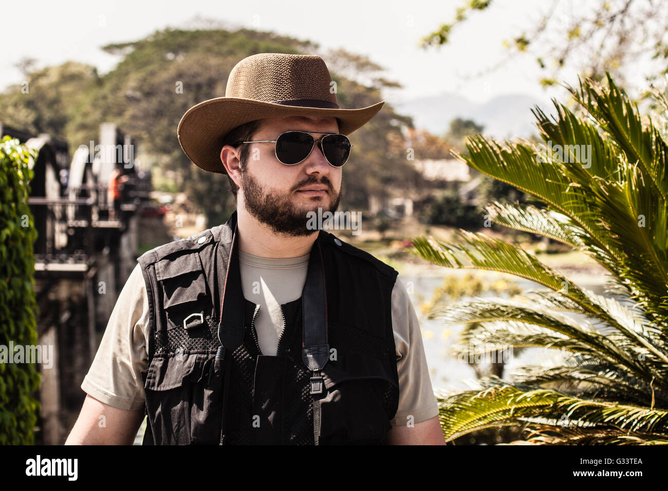 a photographer or adventurer with sunglasses and a stetson near the bridge on the river Kwai Stock Photo