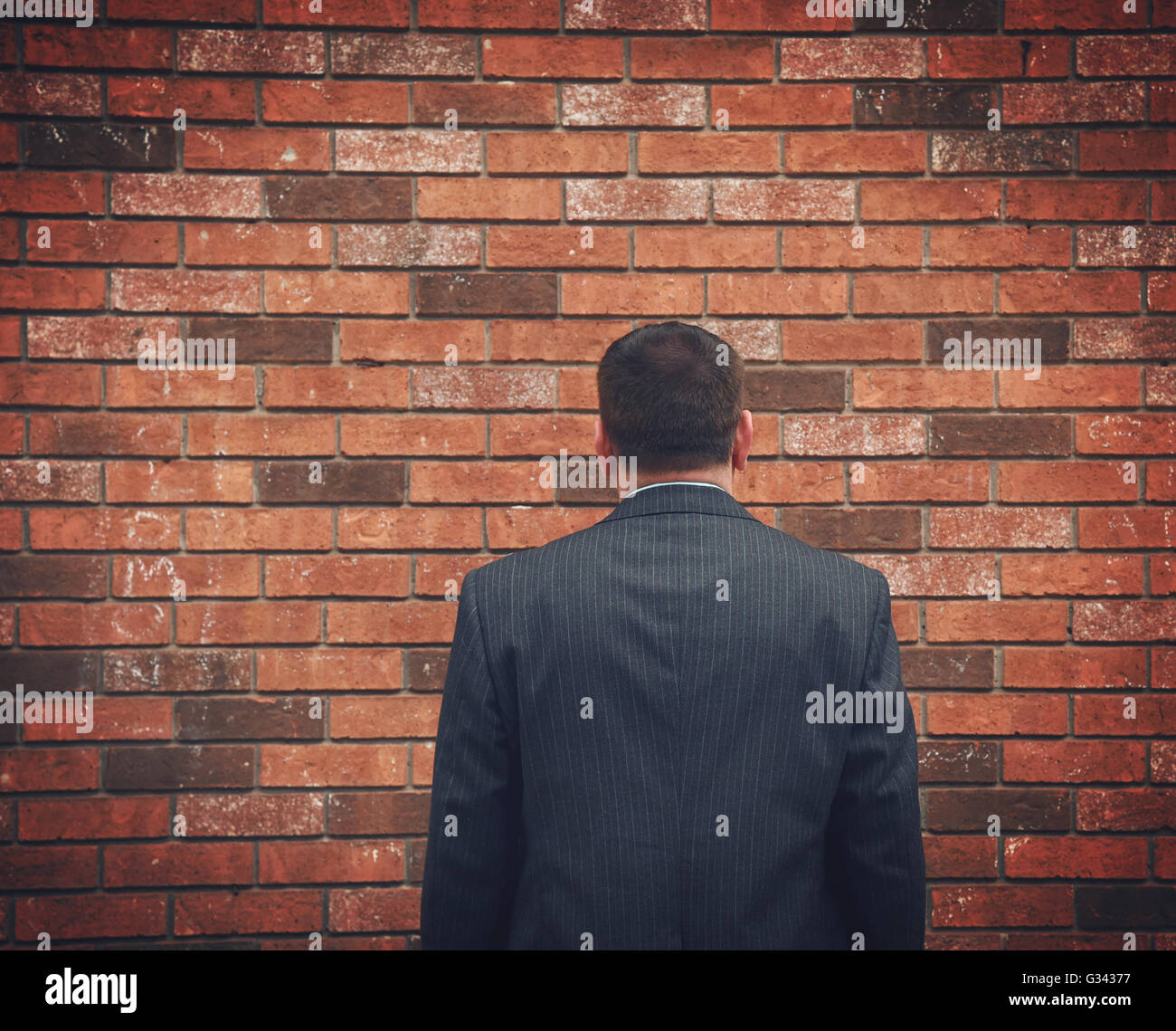 A business man has his back turned and looking at a brick wall. Can represent an obstacle, sadness or a struggle. Stock Photo