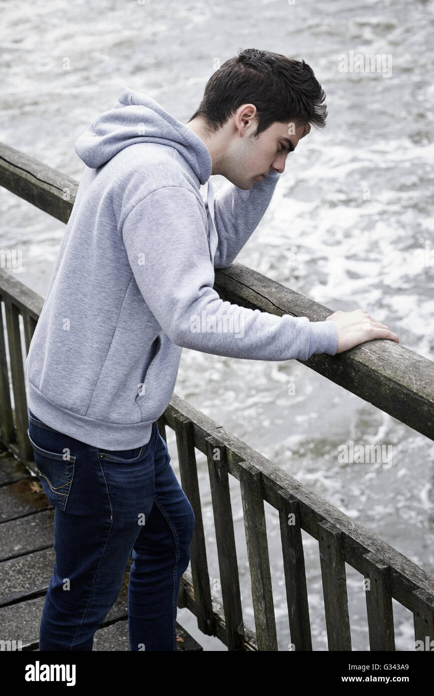 Depressed Young Man Contemplating Suicide On Bridge Over River Stock Photo