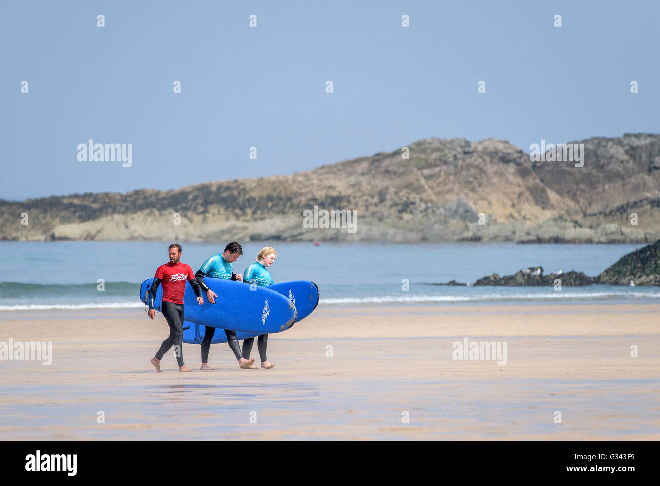 A surfing instructor and his two novice surfers walk along Fistral Beach in Newquay, Cornwall