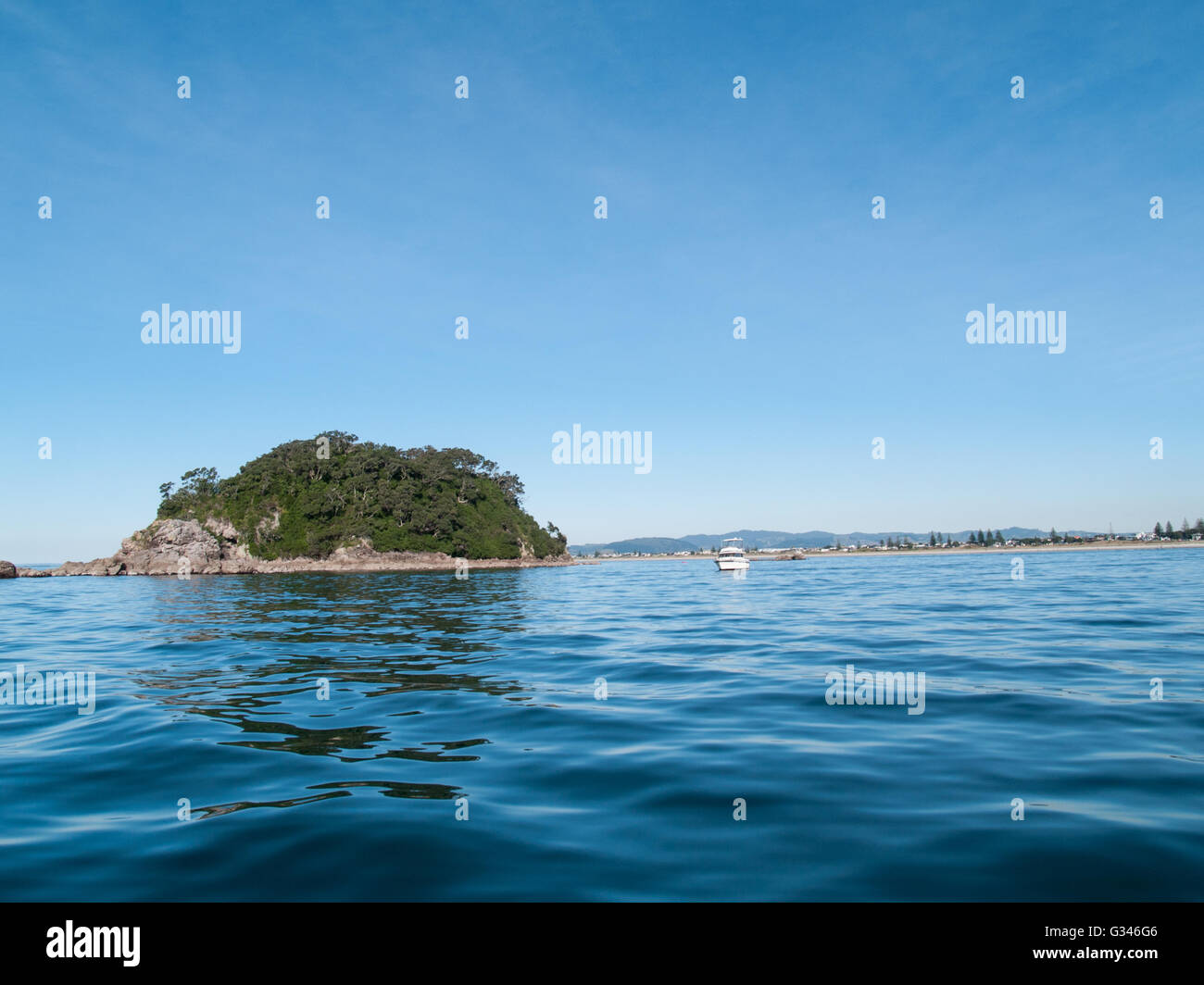 Off-shore island across blue of ocean from low point of view with Mount Maunganui beach background. Stock Photo