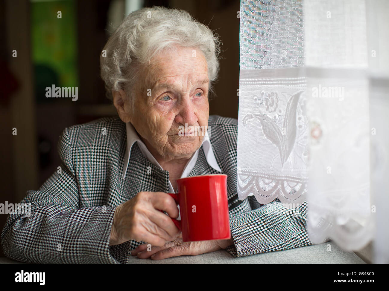 Elderly woman drinking tea sitting at the table. Stock Photo