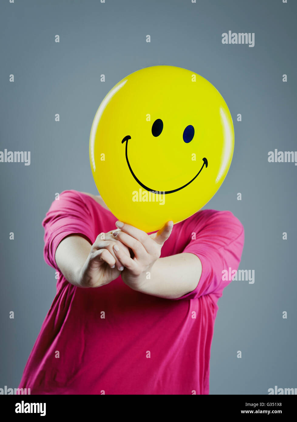 Woman with a smiley face balloon in front of her face Stock Photo