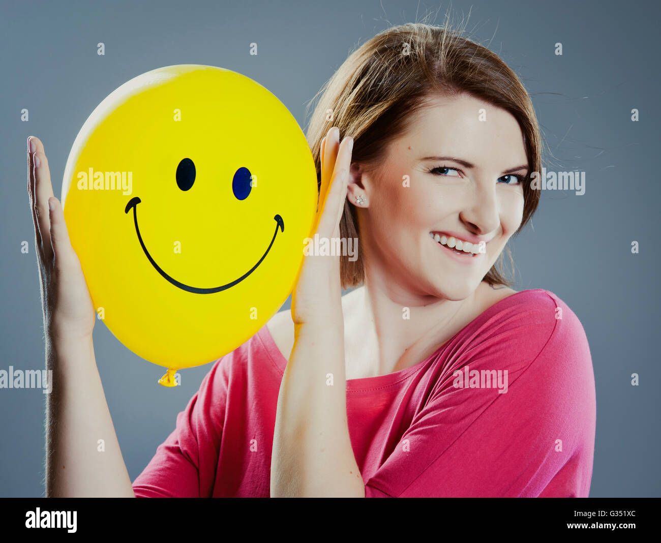 Smiling young woman holding a smiley face balloon Stock Photo
