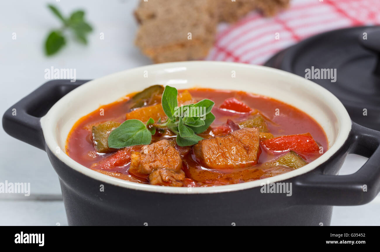 Goulash in a black cocotte with marjoram on white wood. Stock Photo