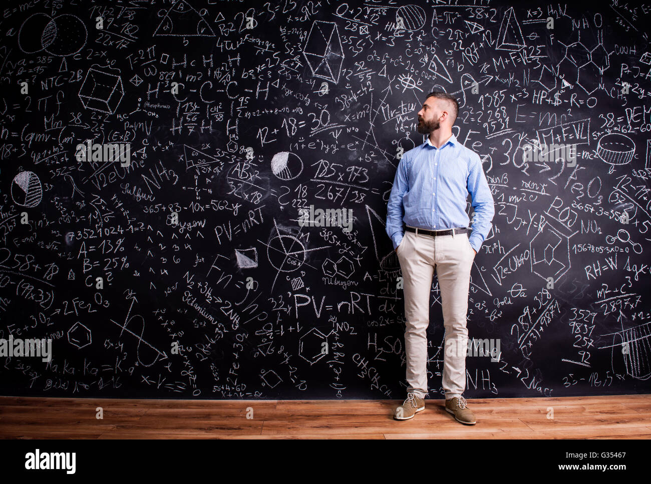 Hipster teacher against big blackboard with mathematical symbols Stock