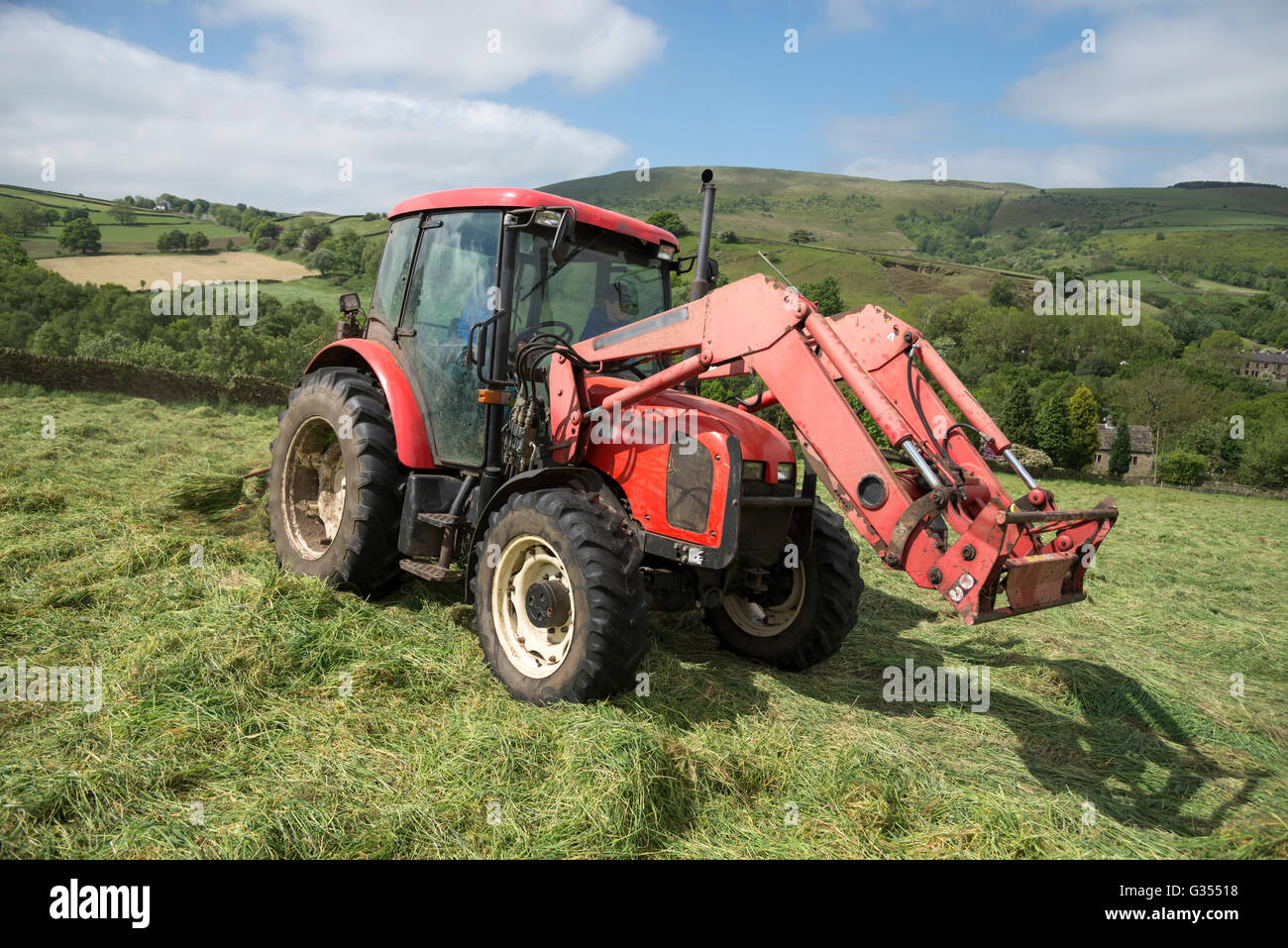 A red tractor turning grass to dry in a summer hay meadow in the
