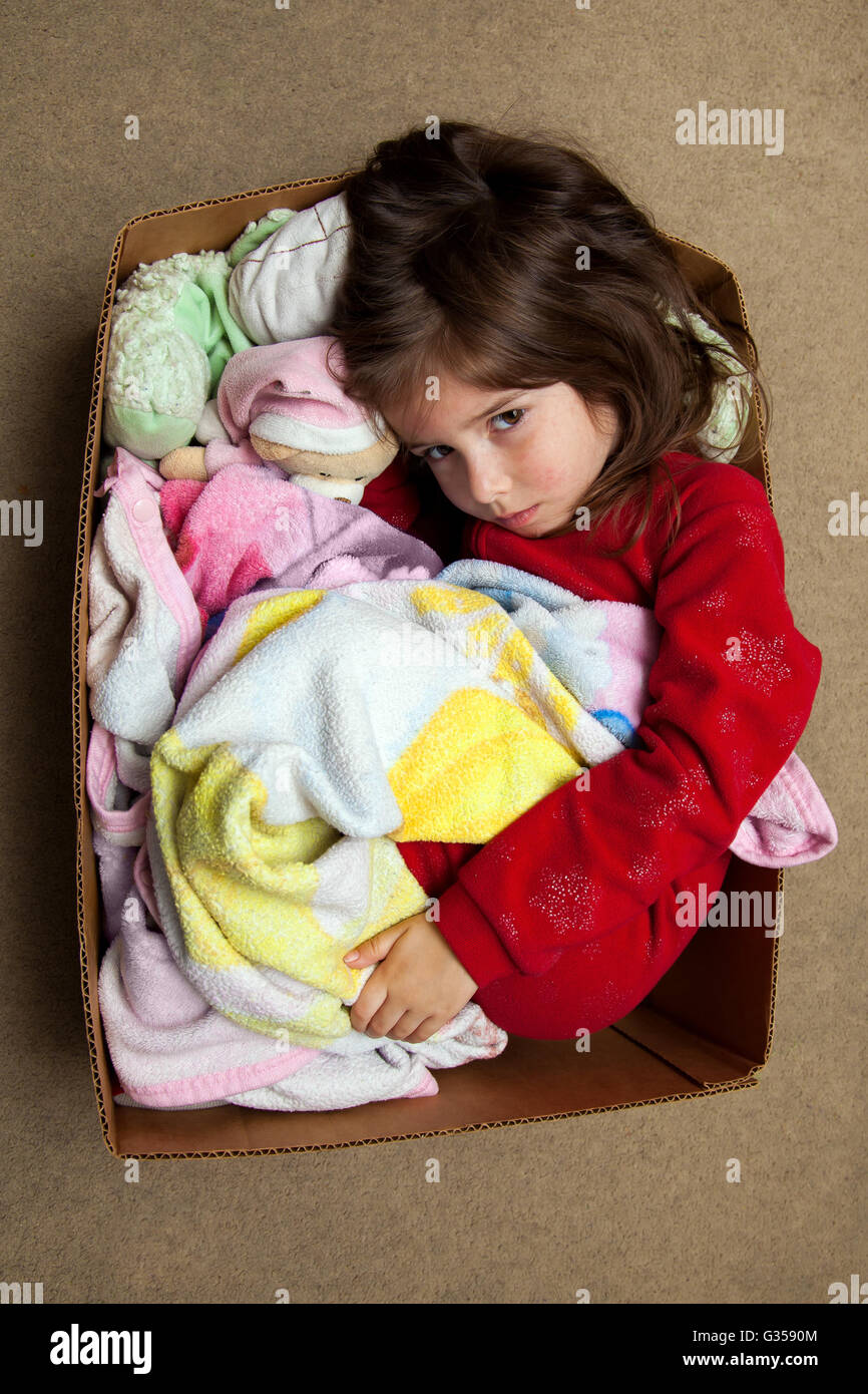 A young girl with a fever rash curls up in a box to cuddle with her blanket an stuffed animals. Stock Photo
