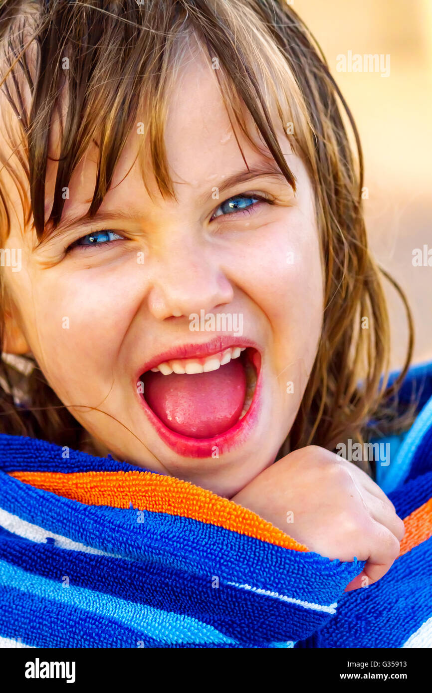 A happy girl wrapped in a beach towel looks at the camera with open