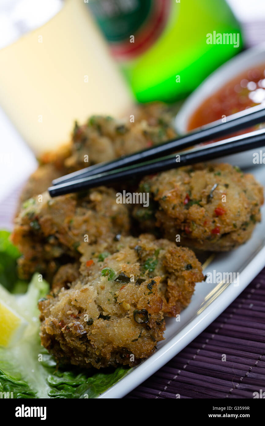 A traditional serving of Thai Fish Cakes (tod man pla) presented with an accompaniment of Cucumber Relish and a glass of beer. Stock Photo