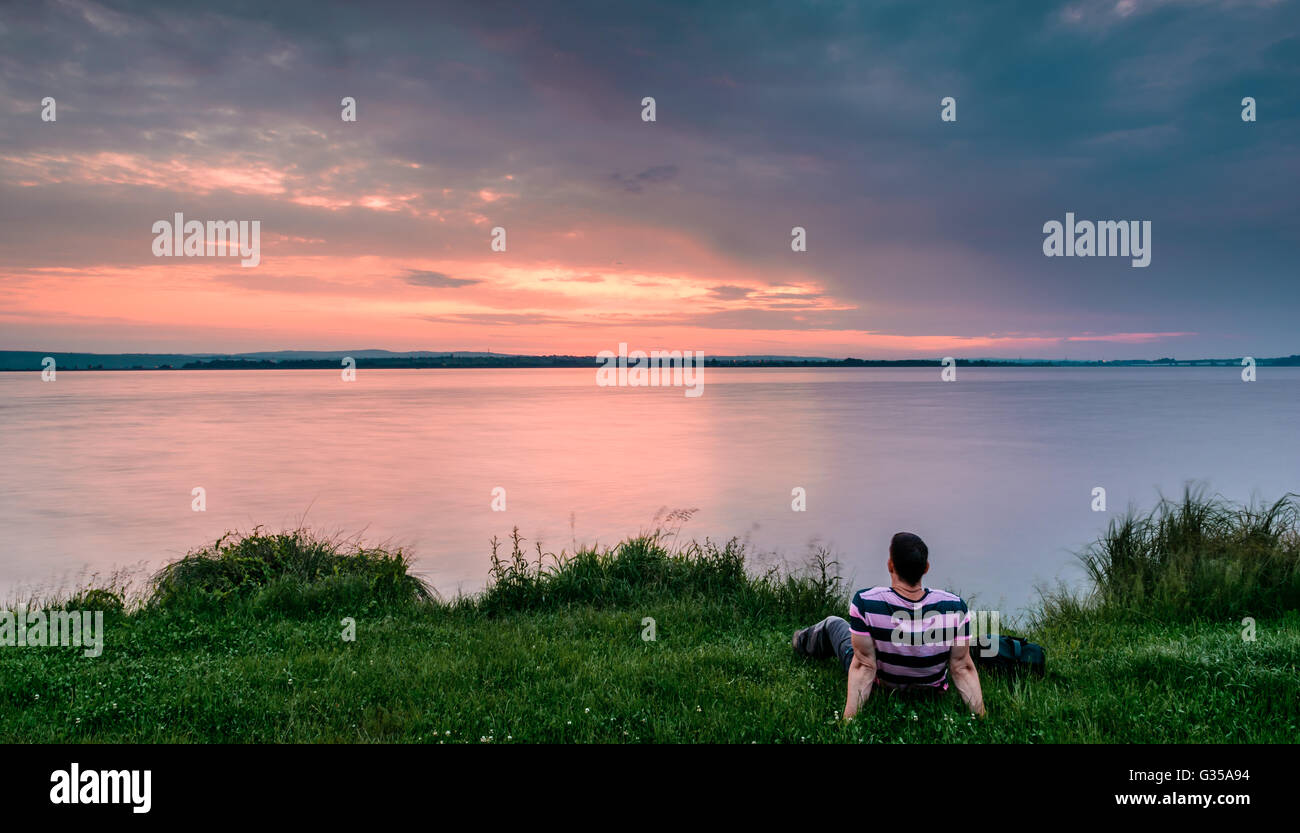 Man sitting and looking to beautiful sunrise behind the lake Stock Photo