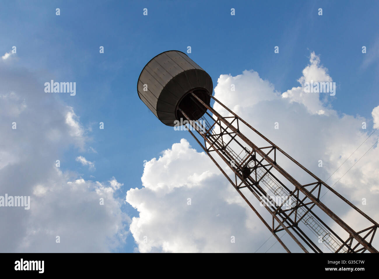 An old rusty water tower over a cloudy blue sky Stock Photo - Alamy
