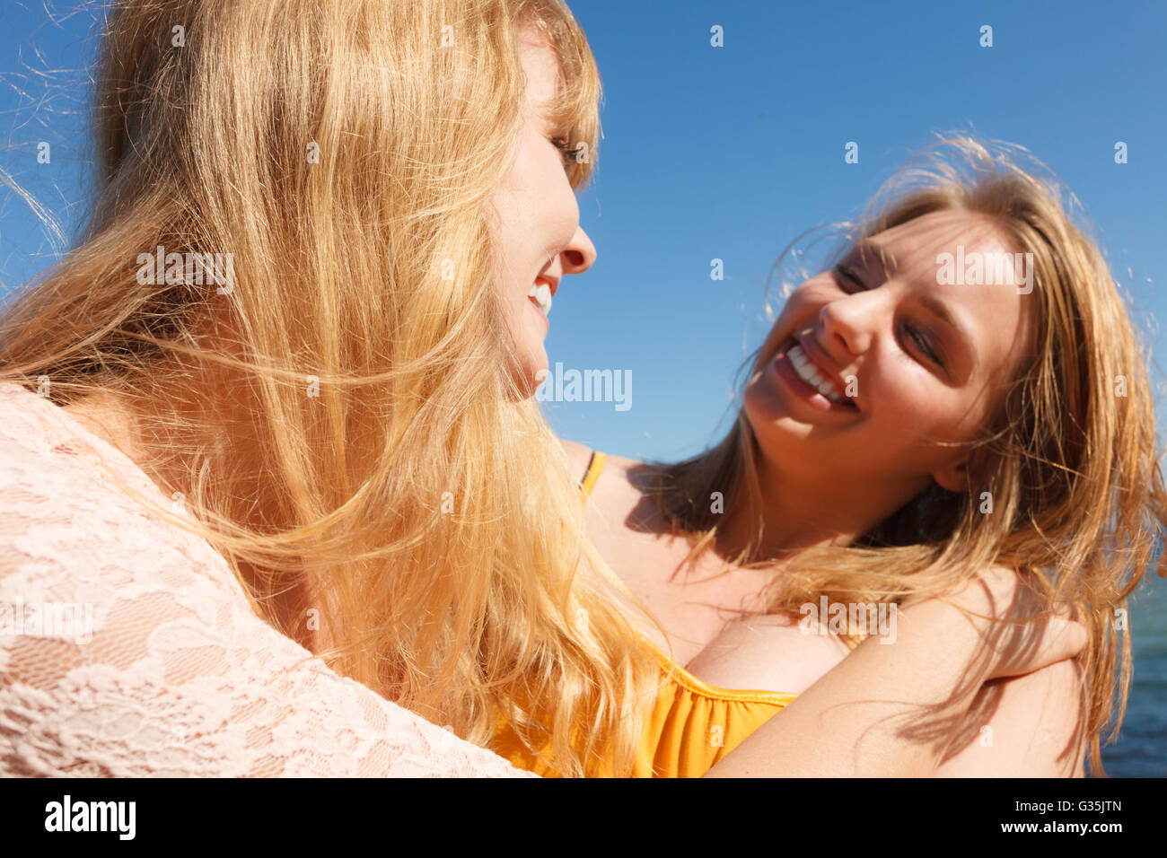 Two young women best friends blonde cheerful girls having fun outdoor against blue sky wind blowing in hair. Summer happiness friendship concept. Stock Photo