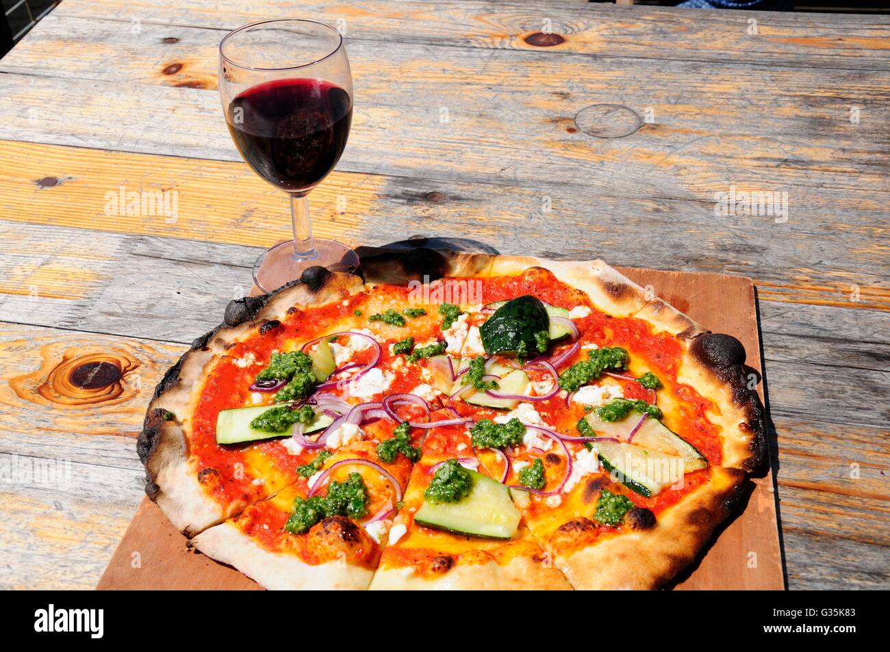 Wood fired vegetarian pizza and a glass of red wine on a rustic wooden table Stock Photo