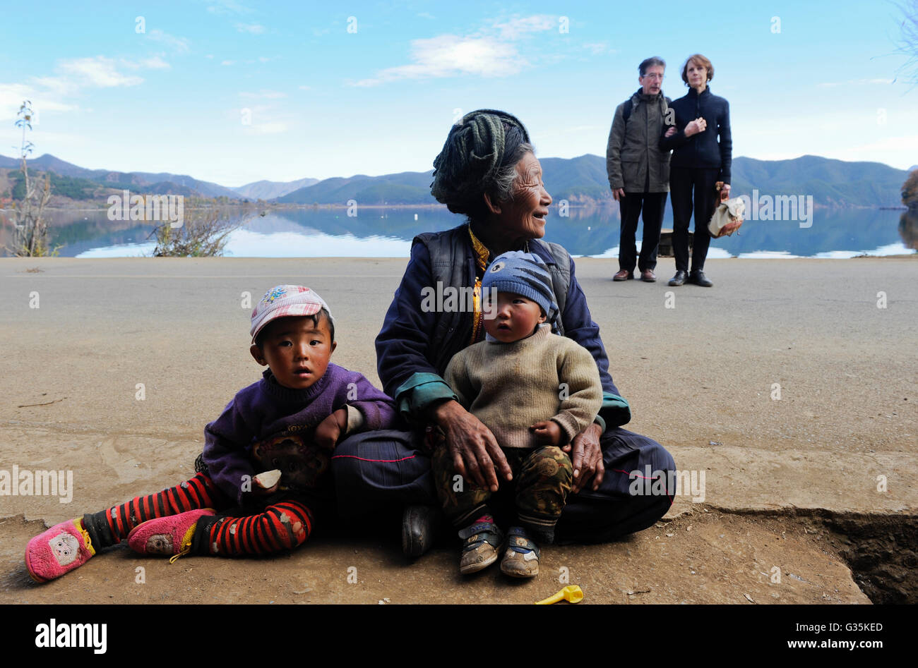 CHINA province Yunnan Lugu Lake , ethnic minority Naxi, old woman with children, two french tourist , culture clash Stock Photo
