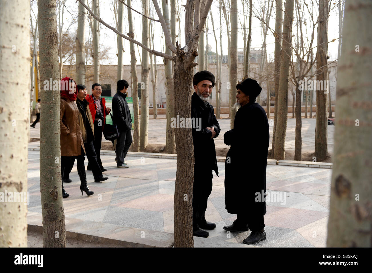 CHINA province Xinjiang, city Kashgar, where uyghur people are living , Heytgar or Idkah mosque, two uighur men wearing a fur hat and Han-chinese tourists, Id Kah mosque is the largest mosque in China and may accommodate up to 20,000 worshipper Stock Photo
