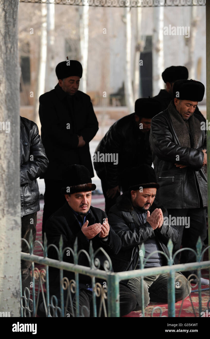 CHINA province Xinjiang, city Kashgar, where uyghur people are living , Heytgar or Idkah mosque, muslim men at prayer, uighur men wear a fur hat, Id Kah mosque is the largest mosque in China and may accommodate up to 20,000 worshipper Stock Photo