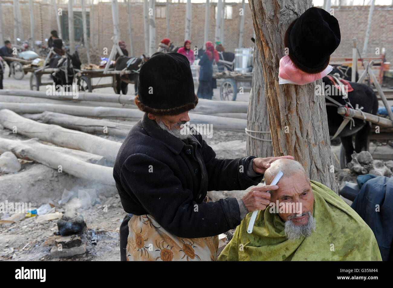 CHINA, province Xinjiang, market day in uighur village Jin Erek near city Kashgar where uyghur people are living, open air barber shop, head and beard shaving during freezing temperatures Stock Photo
