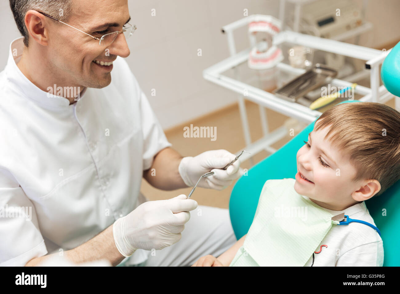 Smiling dentist in glasses doing dental treatment to little boy Stock