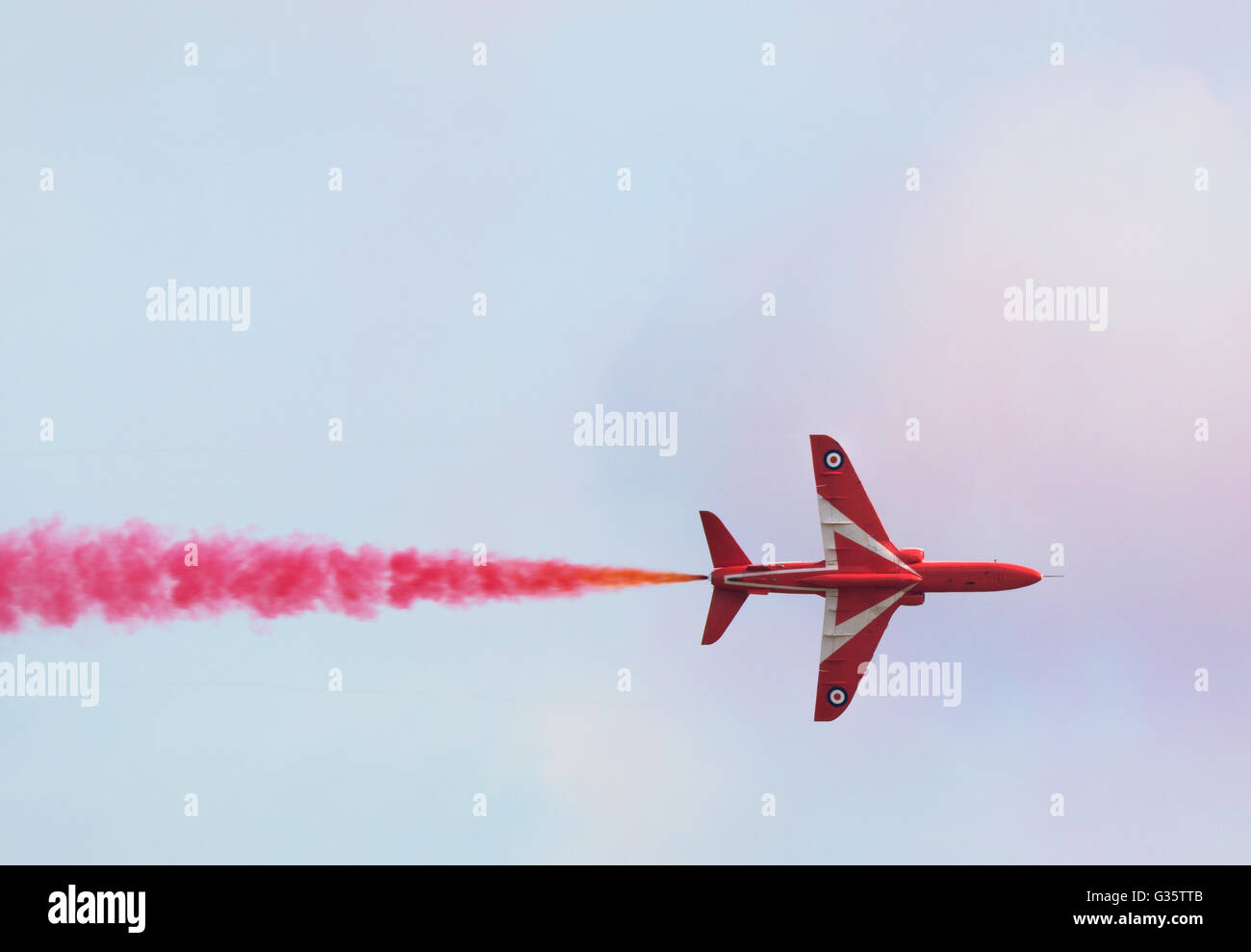 RAF Red Arrows plane flying straight, with colourful red smoke, Duxford Airshow, Cambridgeshire UK Stock Photo