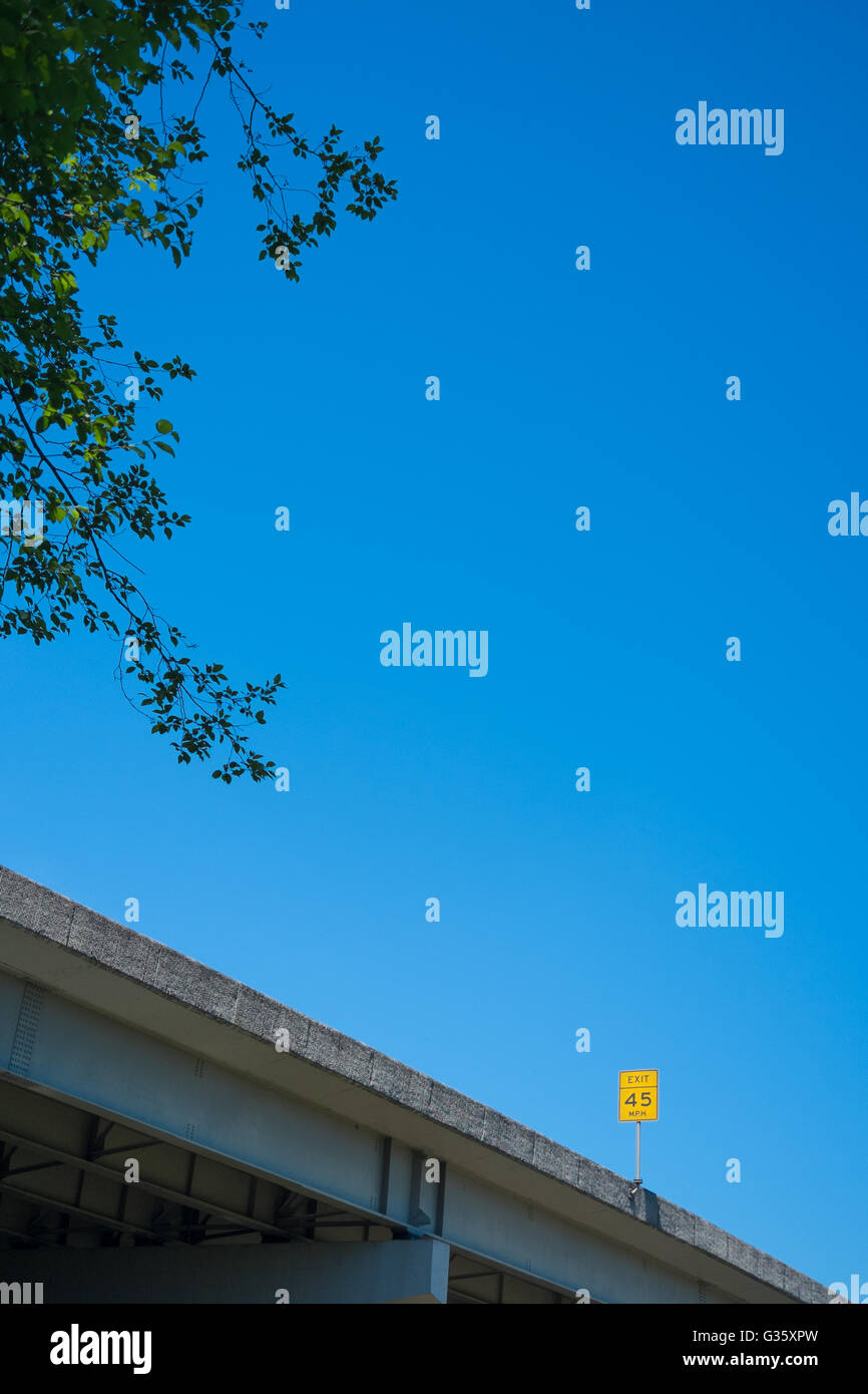 A yellow 45mph Freeway Exit Sign with trees and blue skies shot from a low angle in the USA Stock Photo
