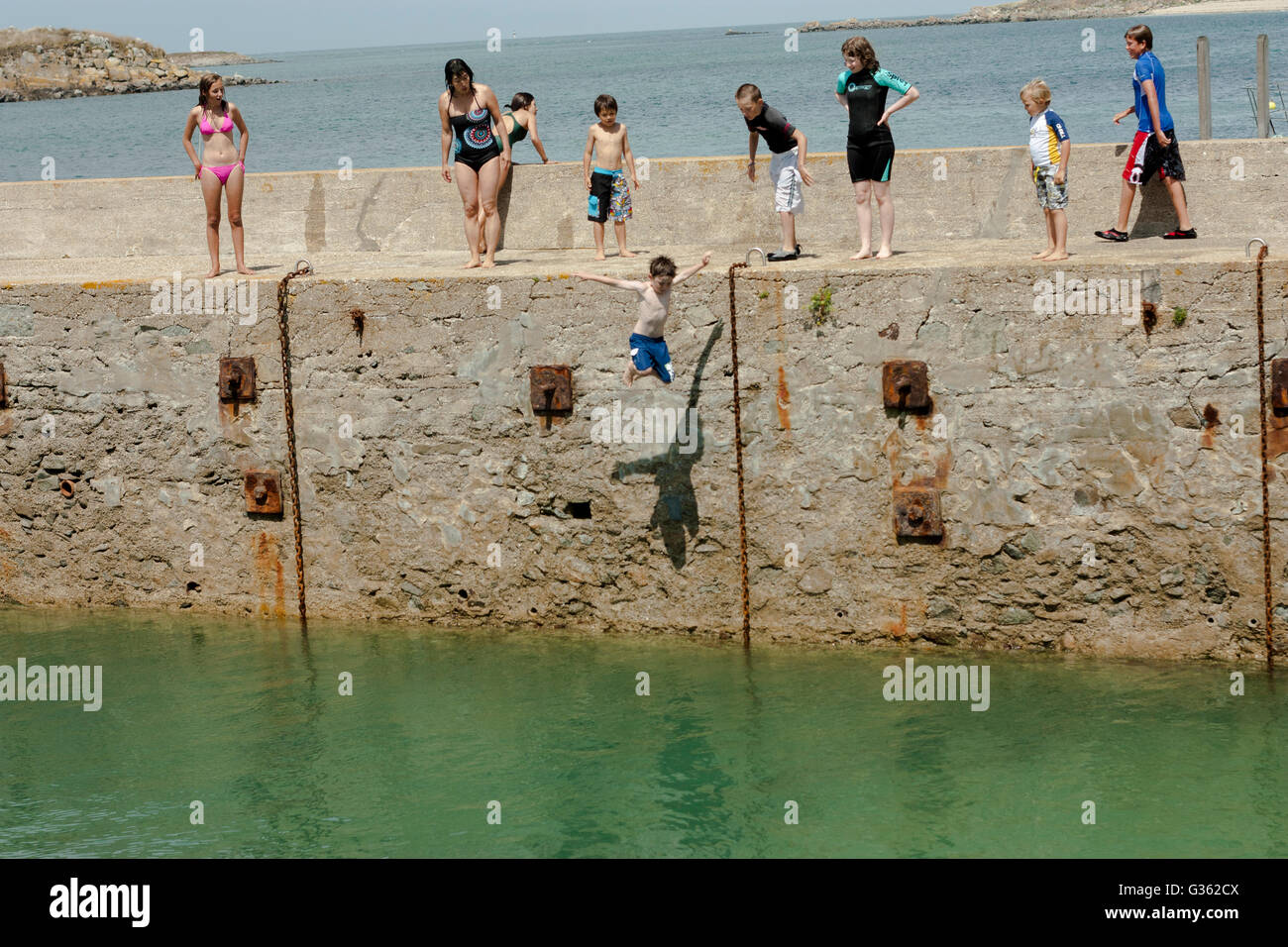 Boys and girls jumping from the jetty into the sea at the harbour in Herm Island, Channel Island Stock Photo