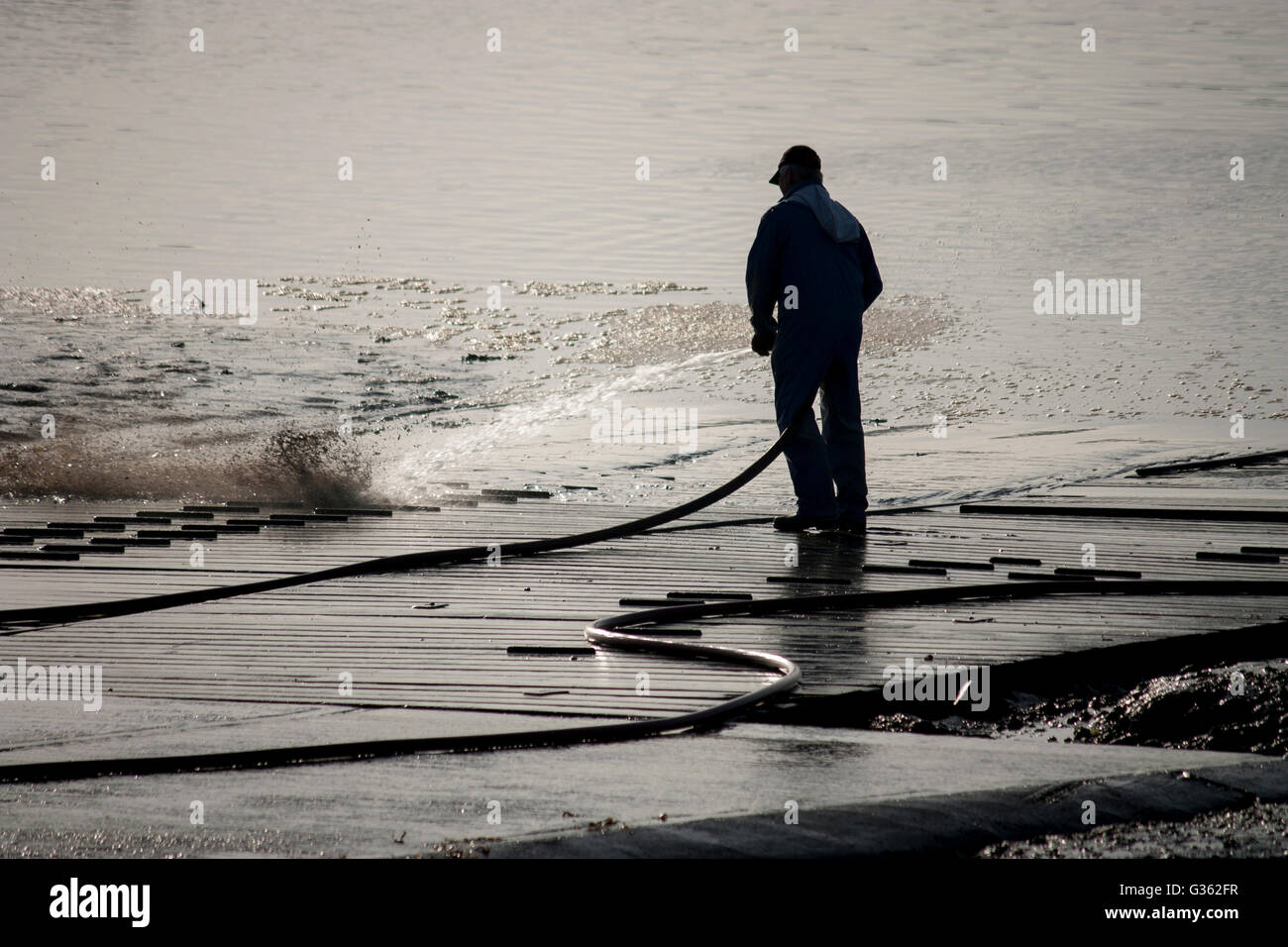 A man using a water hose to wash down a slipway at Upnor, Kent. Stock Photo
