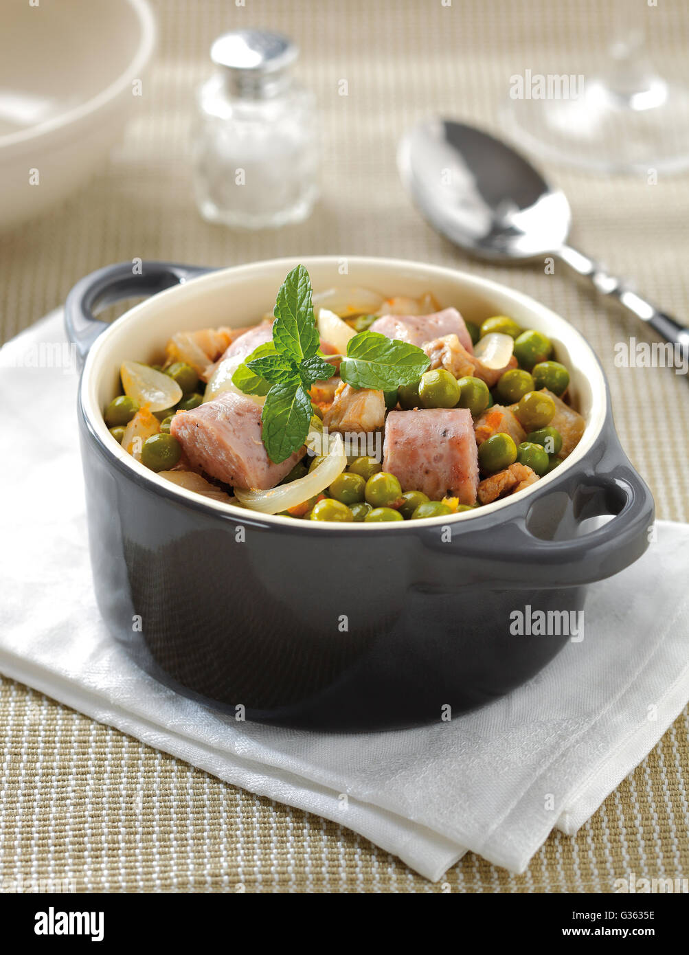 Green pea stew in a small ceramic cooking pot with onions, carrot and sausage. Stock Photo