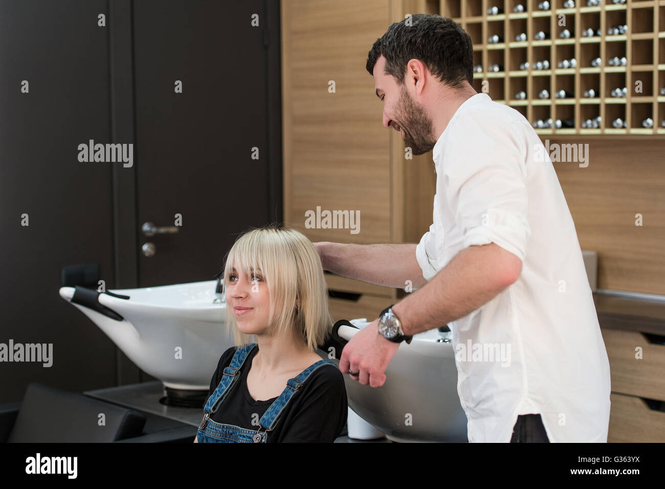 Cheerful dark-haired man doing hairstyle for teen blonde girl in hairdressing saloon Stock Photo