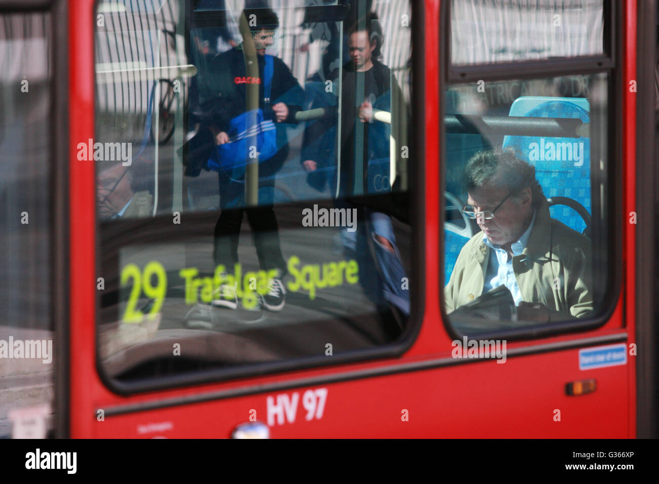 A view of a man reading a newspaper on a London bus and reflections in its windows. Stock Photo