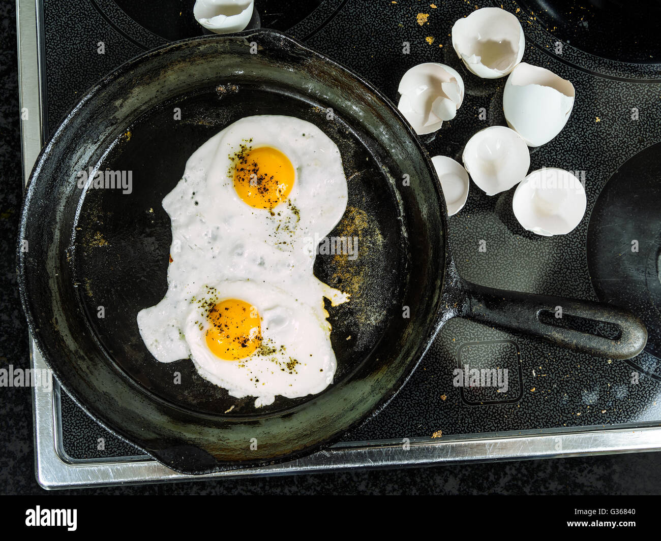 Photo of two eggs frying in a cast iron skillet on top of a stove with egg shells to the side. Stock Photo