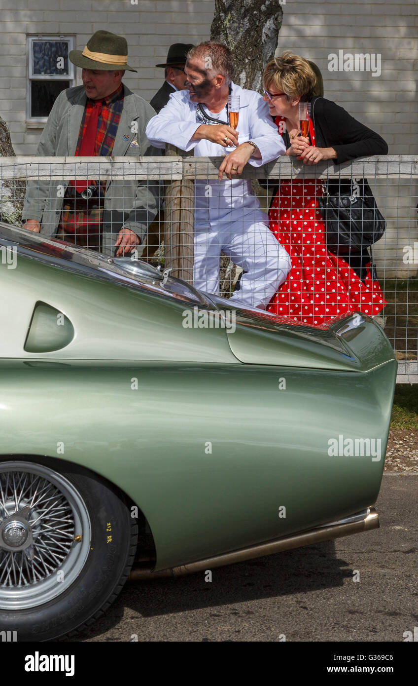Visitors in period dress with drinks beside an Aston Martin at the 2015 Goodwood Revival, Sussex, UK. Stock Photo