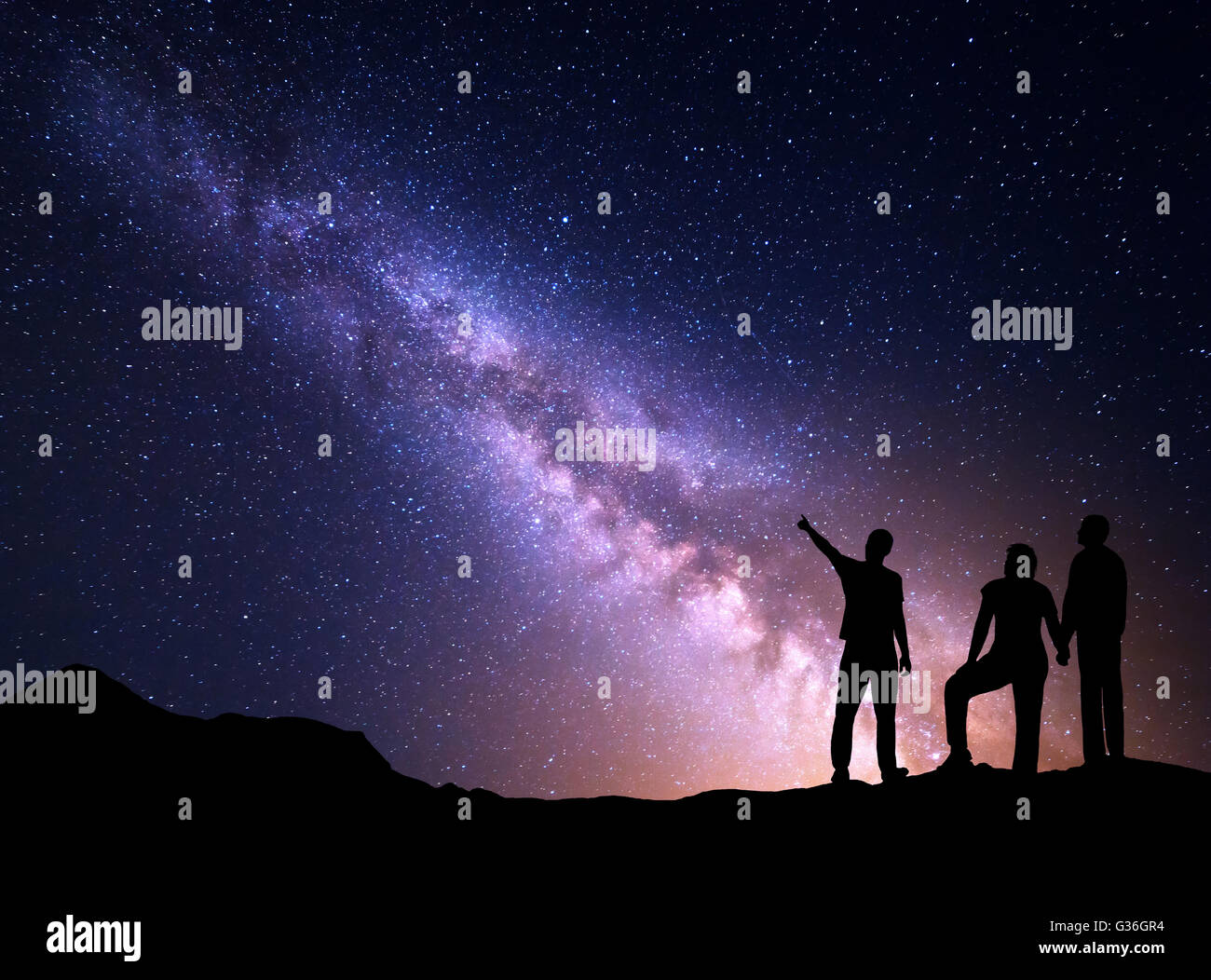 Milky Way with silhouette of a standing young man pointing finger in night starry sky and his parents. Colorful night landscape. Stock Photo