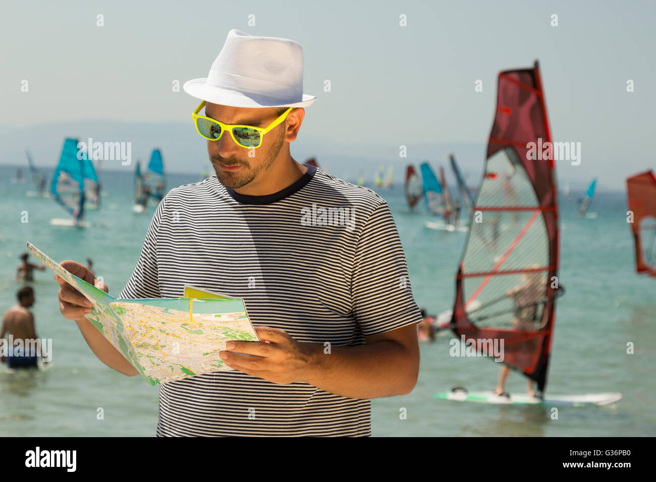 Young tourist guy looking at street map and wind surfers in the background Stock Photo