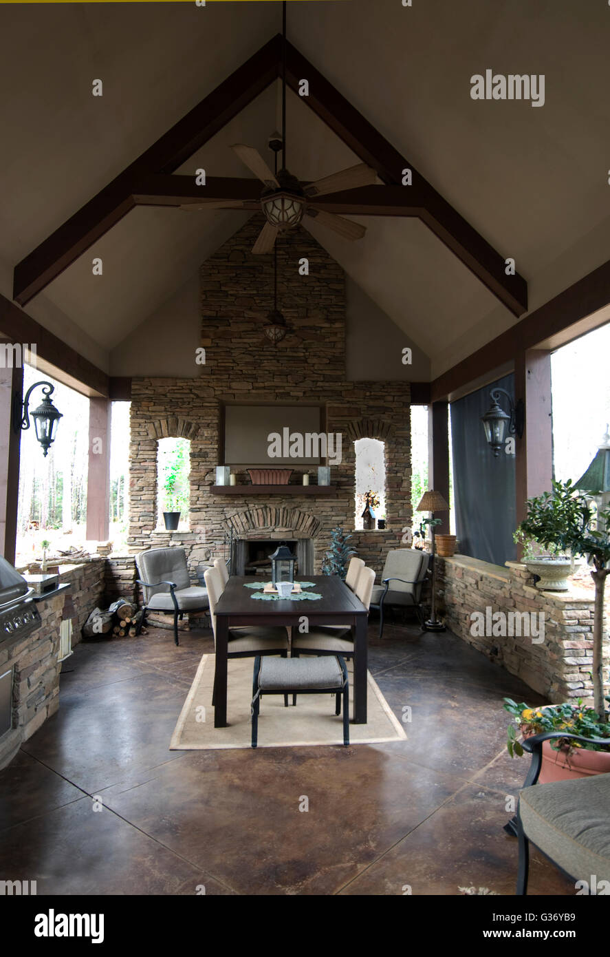 Patio with fireplace , fans, grill, stained concrete floor, stone wall, automatic roller shade, parsons table, Stock Photo