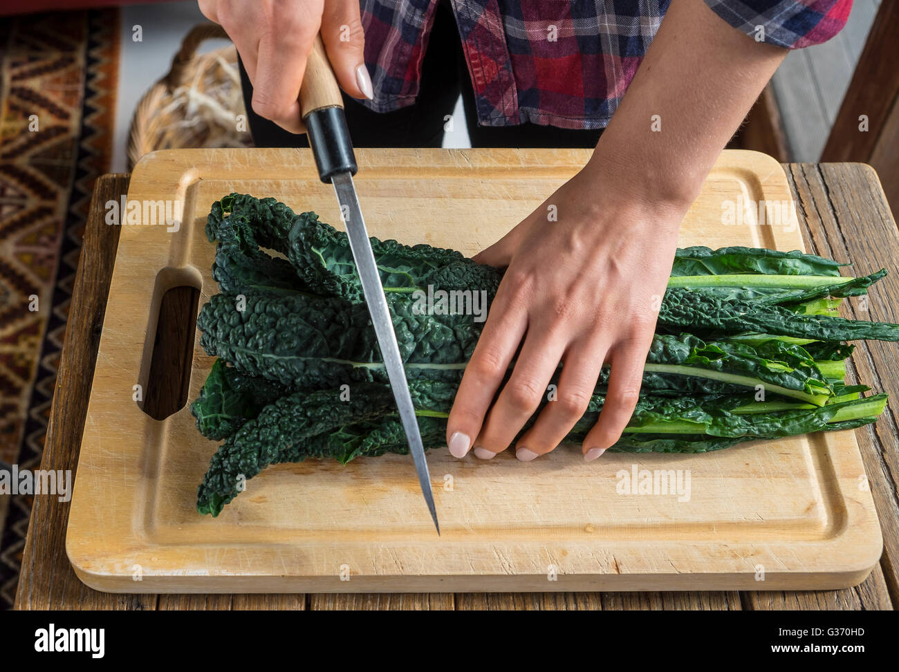 Hands chopping Tuscan kale on a wooden chopping board using a Japanese knife Stock Photo