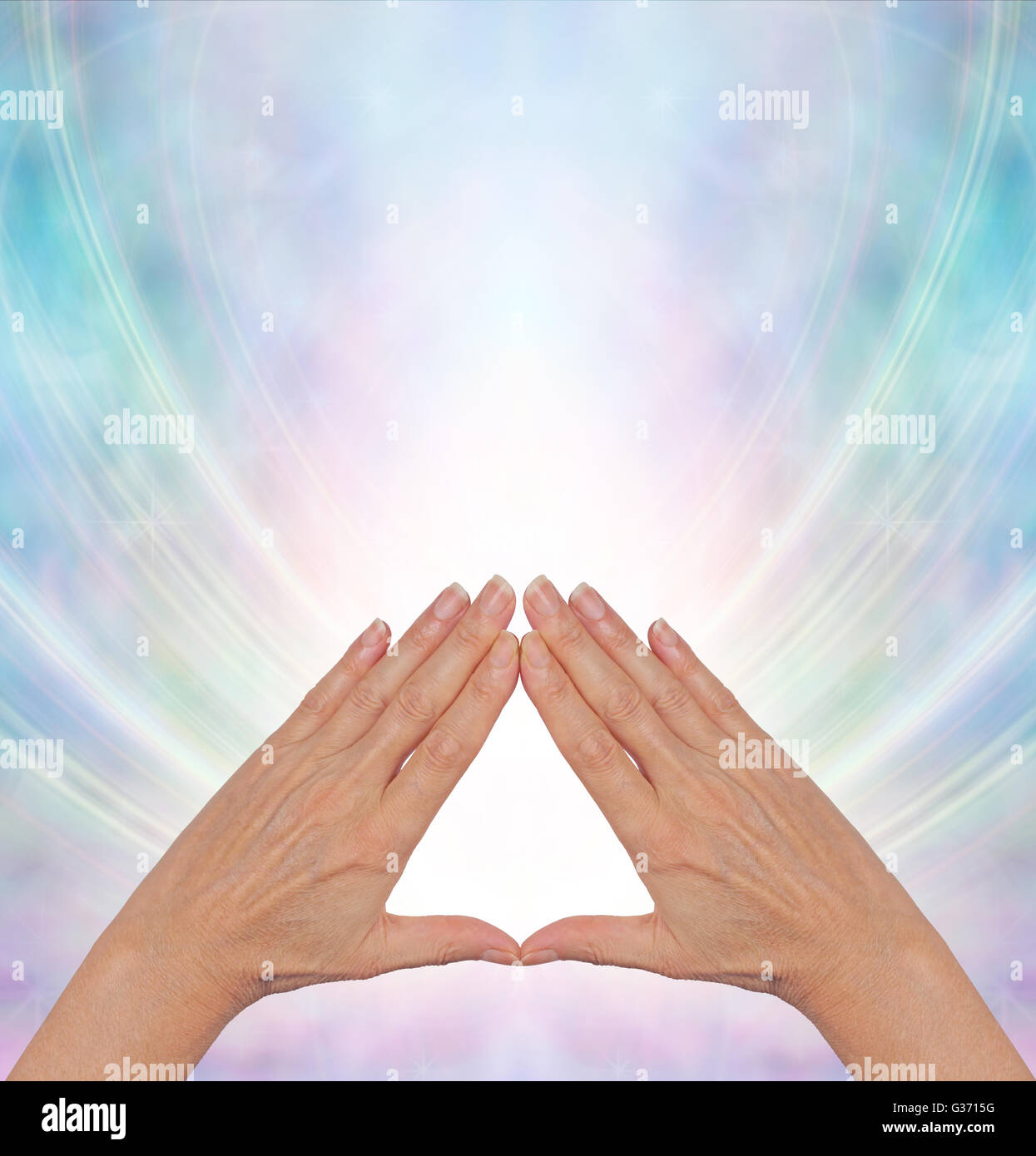 Pyramid healing practitioner with hands in triangle shape wind a shaft of light behind on a pale blue and pink background Stock Photo
