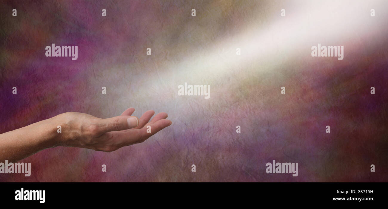 Female hand palm up with a shaft of light coming from top right into palm on rustic stone effect wide background with copy space Stock Photo