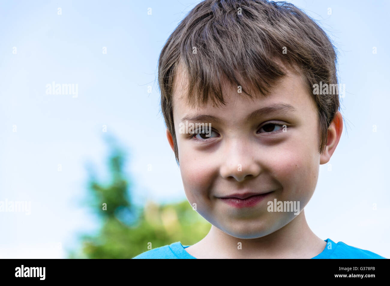 A portrait of a smiling young boy against a blue sky. Stock Photo