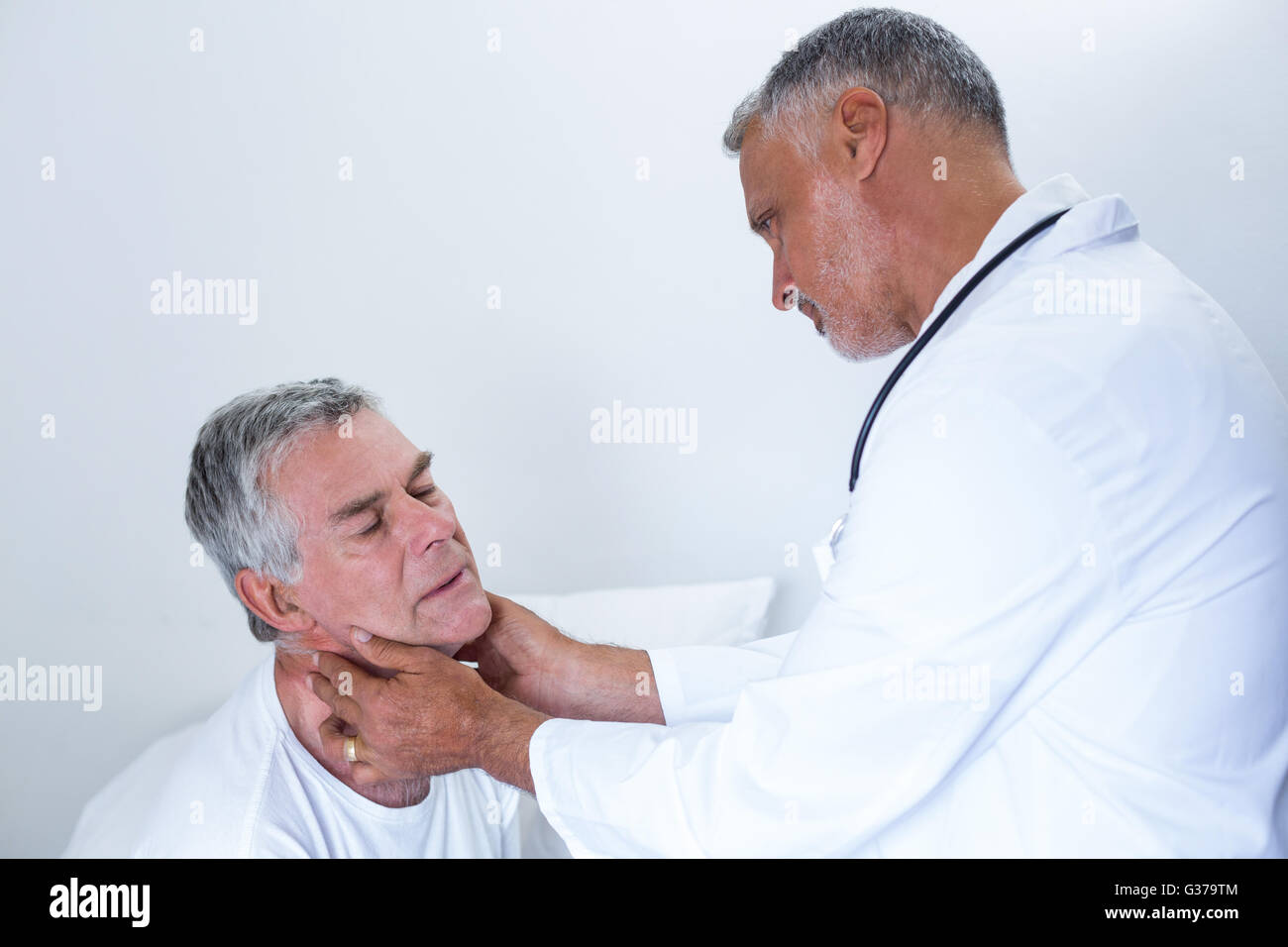 Male doctor examining senior mans neck Stock Photo