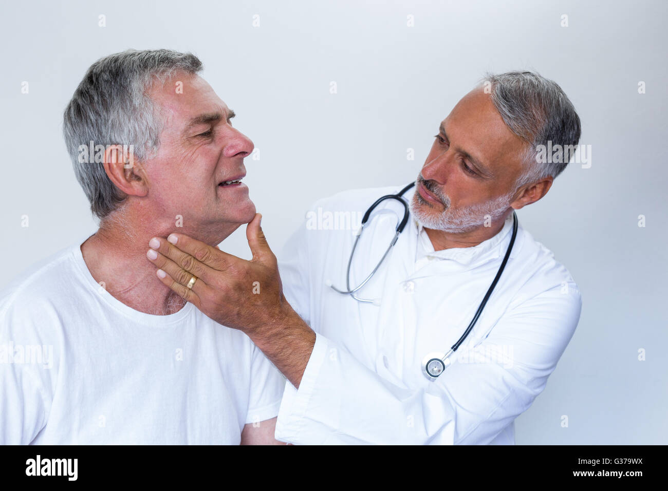 Male doctor examining senior mans neck Stock Photo