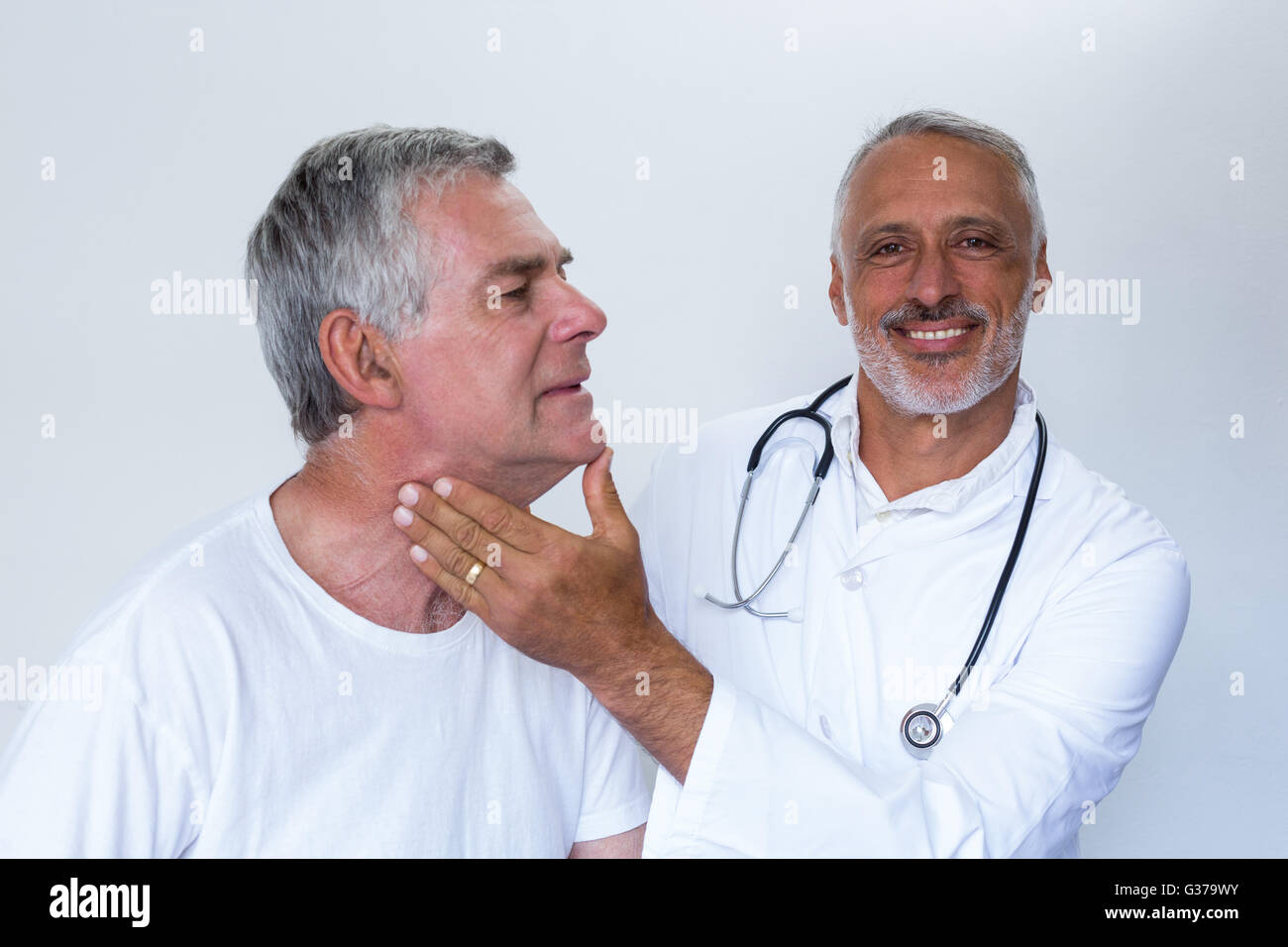 Male doctor examining senior mans neck Stock Photo