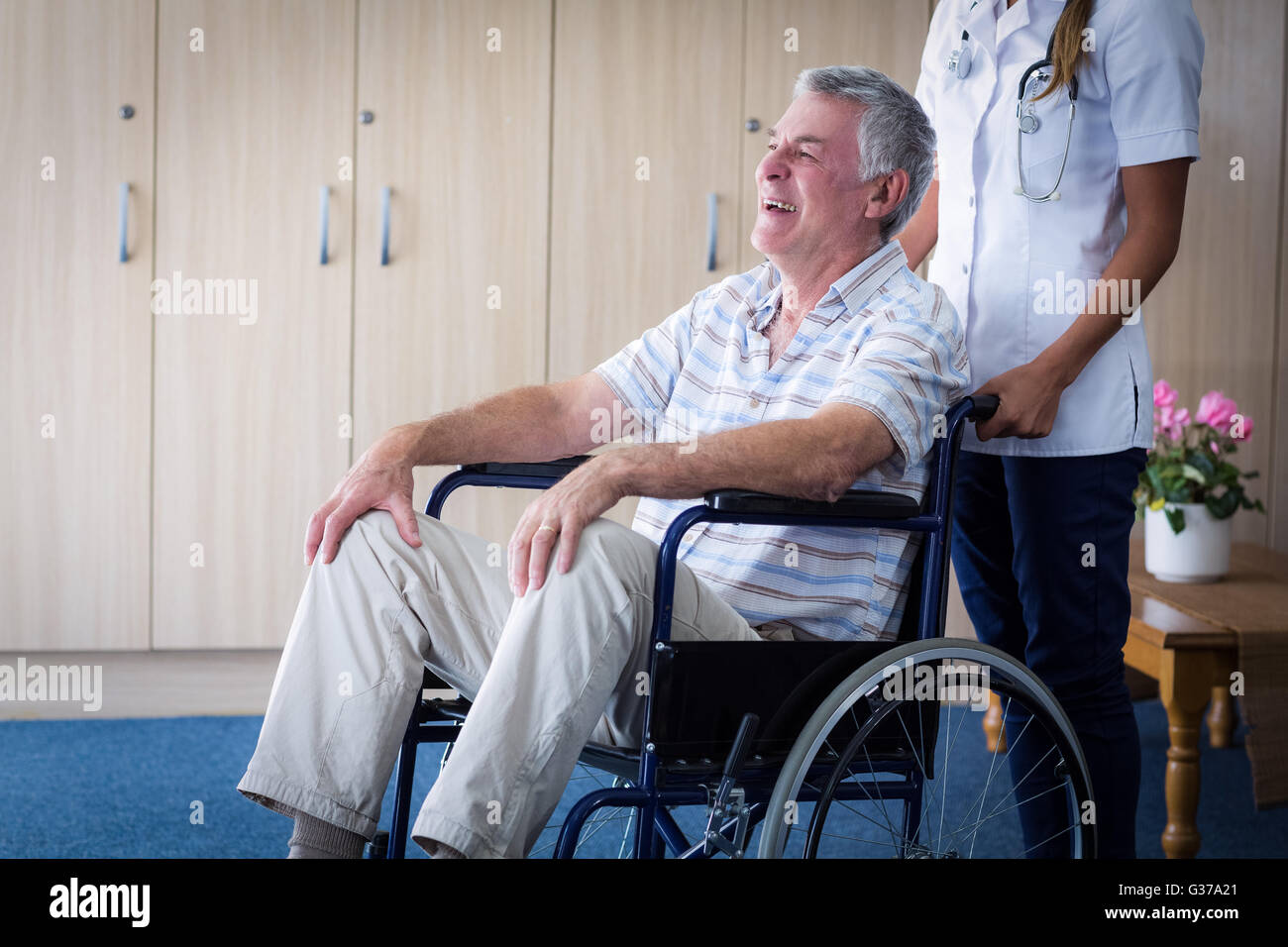 Female doctor carrying senior man on wheelchair Stock Photo