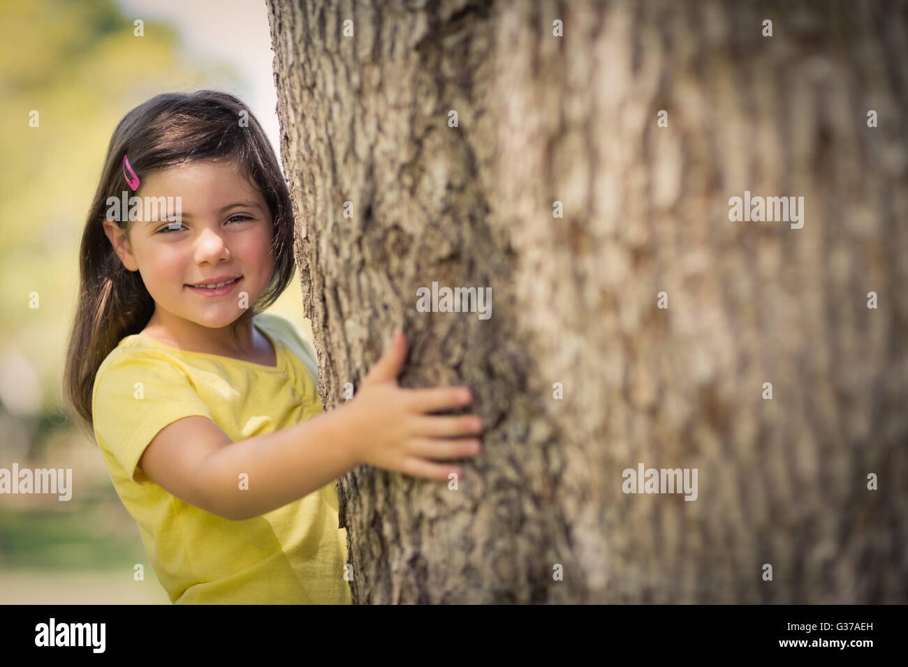 Smiling girl hugging  tree trunk in park Stock Photo