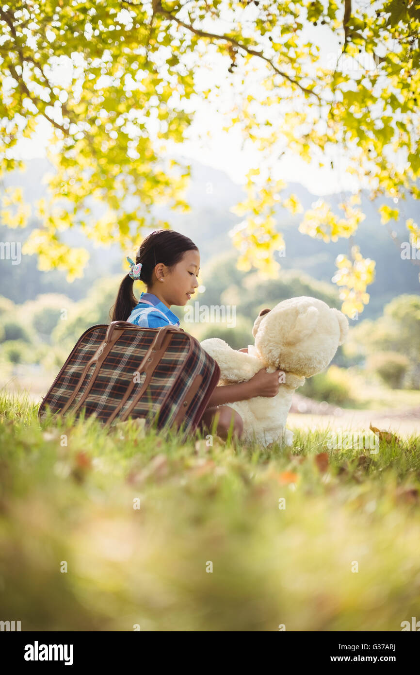 Young girl sitting with a teddy bear and suitcase Stock Photo - Alamy