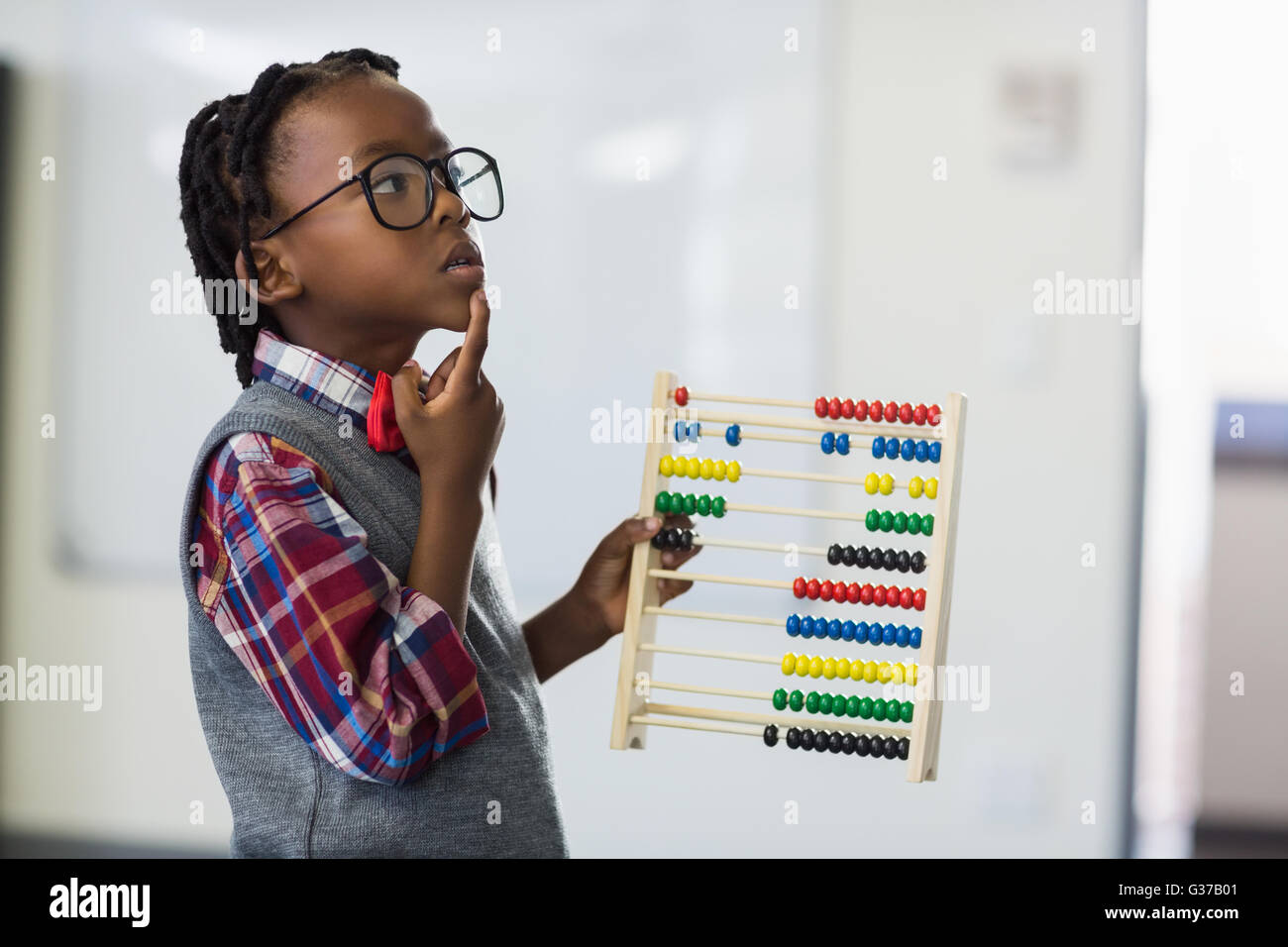 Thoughtful schoolboy using a maths abacus in classroom Stock Photo