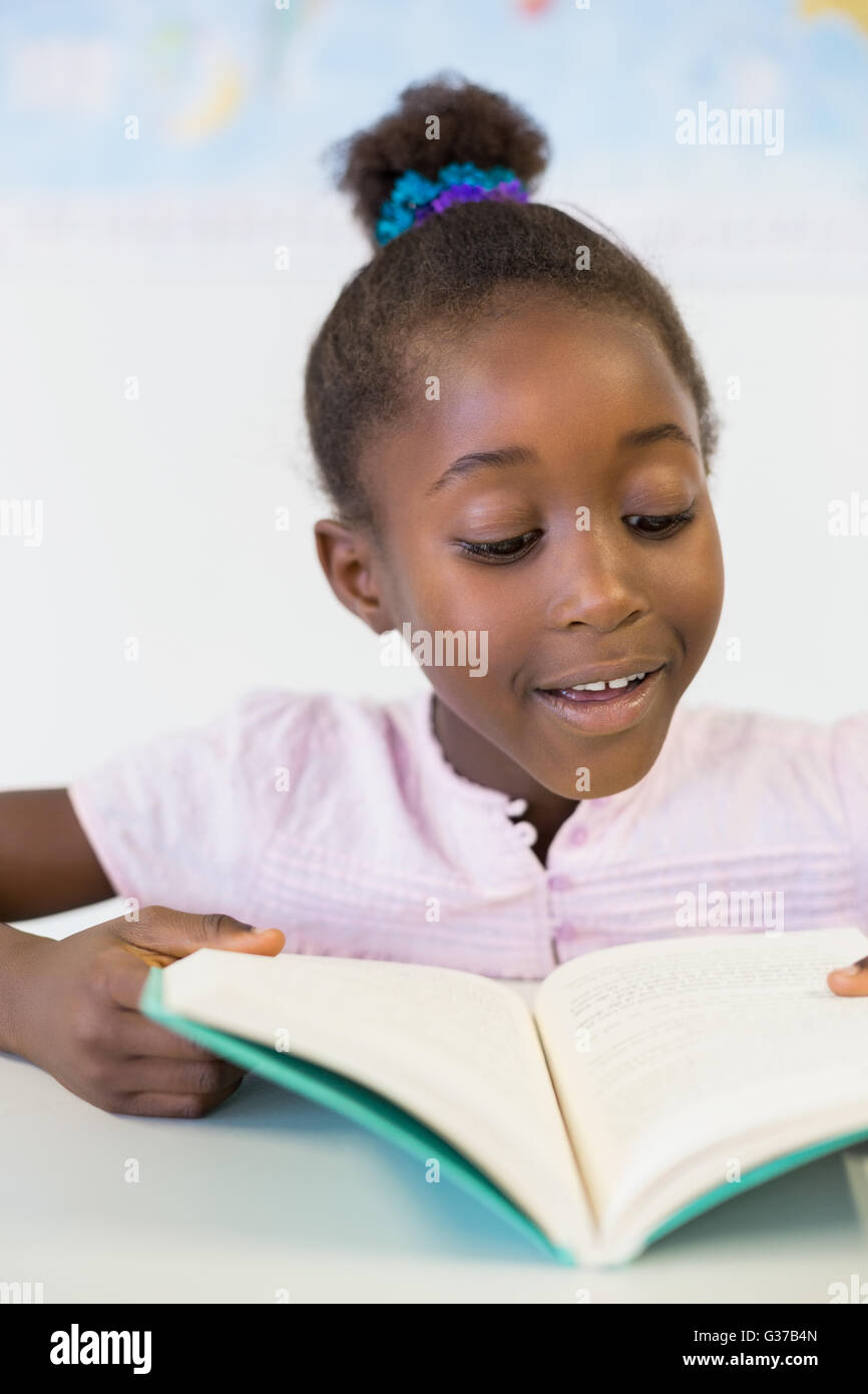 Smiling school girl reading book in classroom Stock Photo - Alamy
