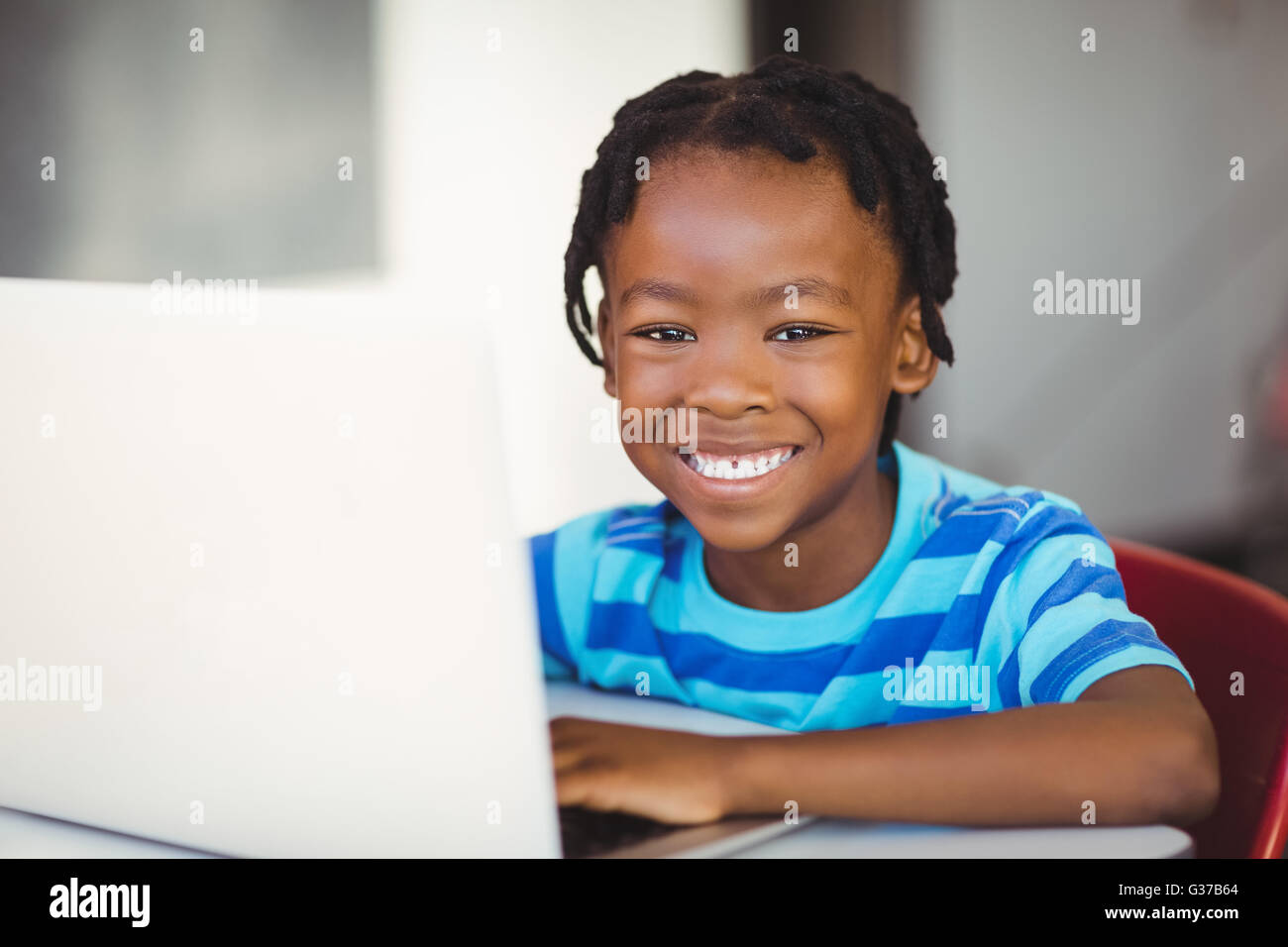 Schoolboy sitting on chair and using laptop at school Stock Photo