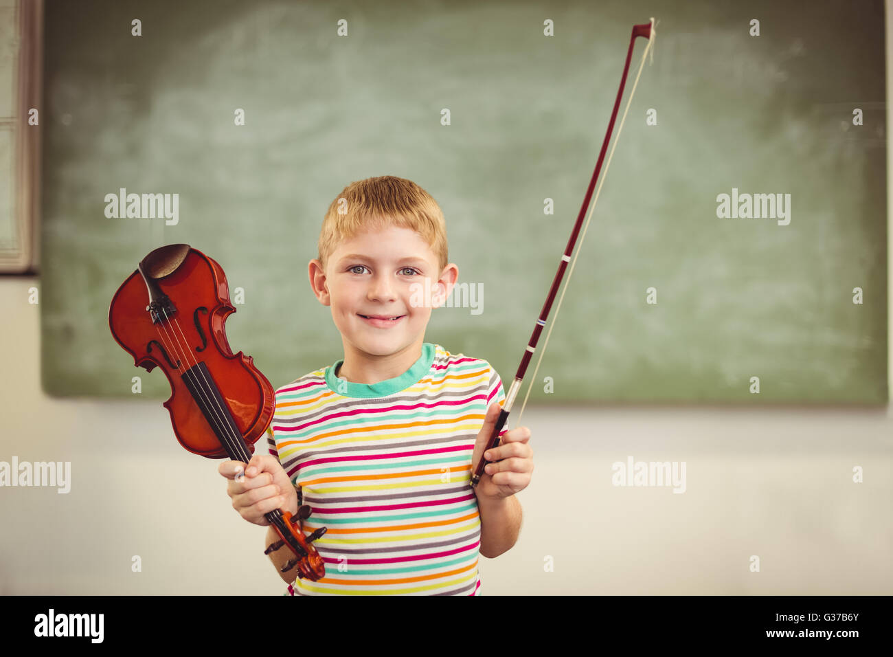 Portrait of smiling schoolboy holding violin in classroom Stock Photo ...