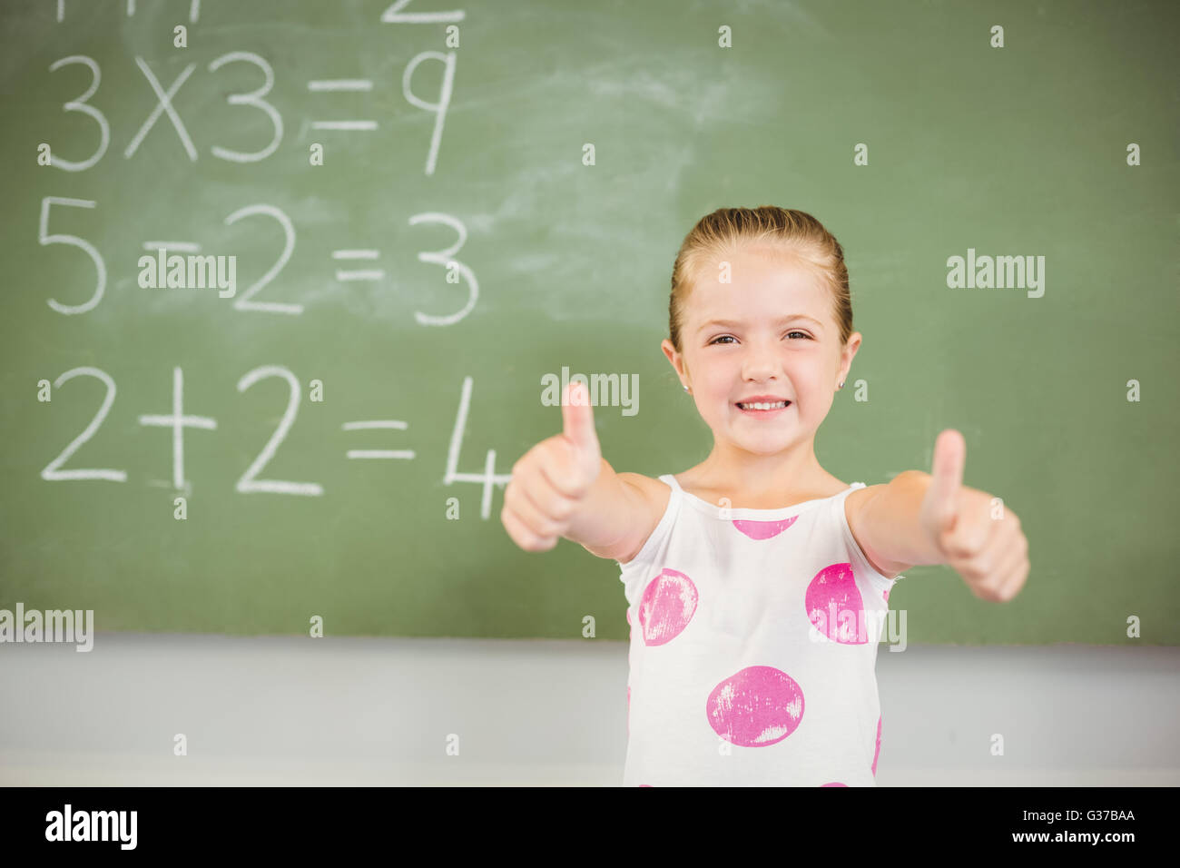 Portrait of smiling schoolgirl showing thumbs up in classroom Stock ...